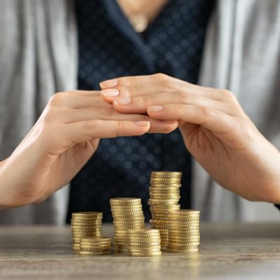 Close up of woman hands covering coins on table. Woman protecting and securing money and savings on wooden table. Safety of savings, investment and insurance concept.