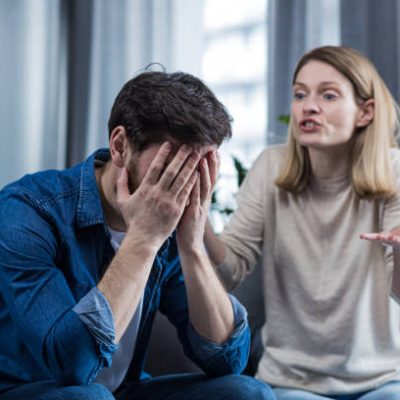Family conflict, quarrel, misunderstanding. The woman shouts at her husband, in despair, crying. requires explanation. The man listens, covering his face with his hands. Sitting on the couch at home.